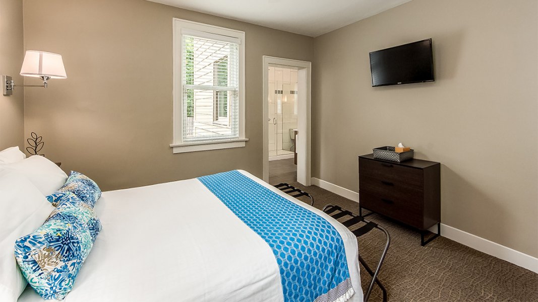 Looking through the bedroom and into the bathroom of a guest suite with bright blue accent pillow on the bed