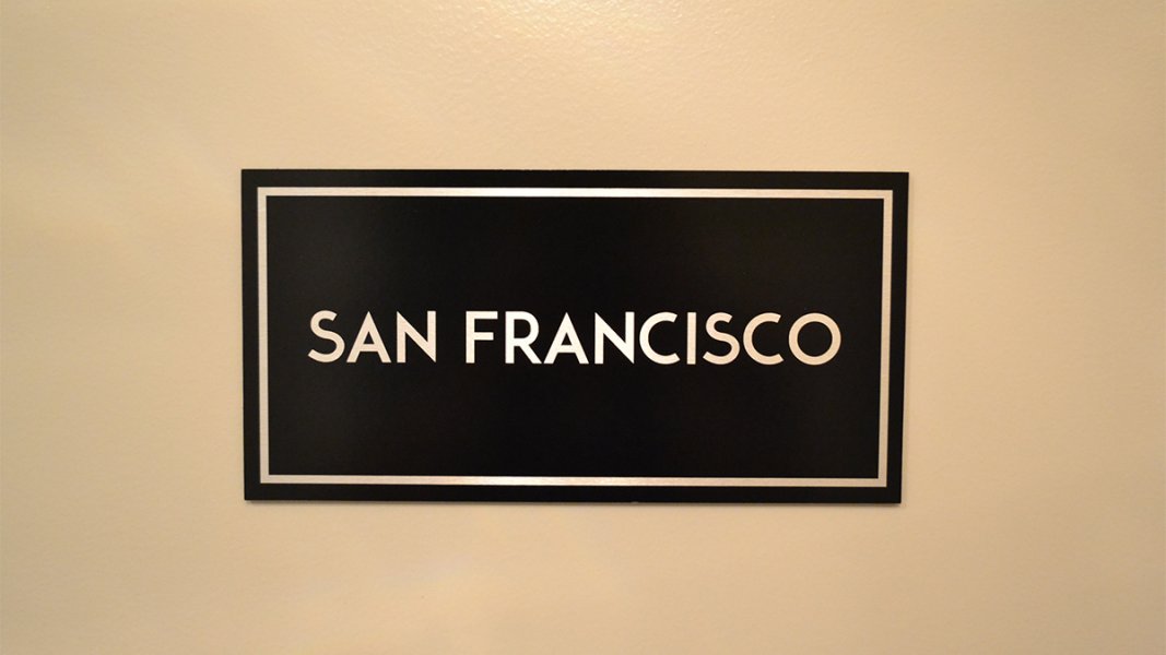 A rectangular sign with black paint and the name of the room showing through in brushed aluminum