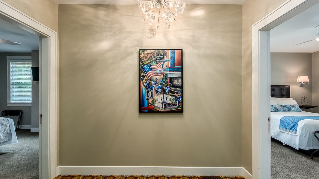 A hallway view of two of the rooms with a modern chandelier and a colorful collage painting by a local artist