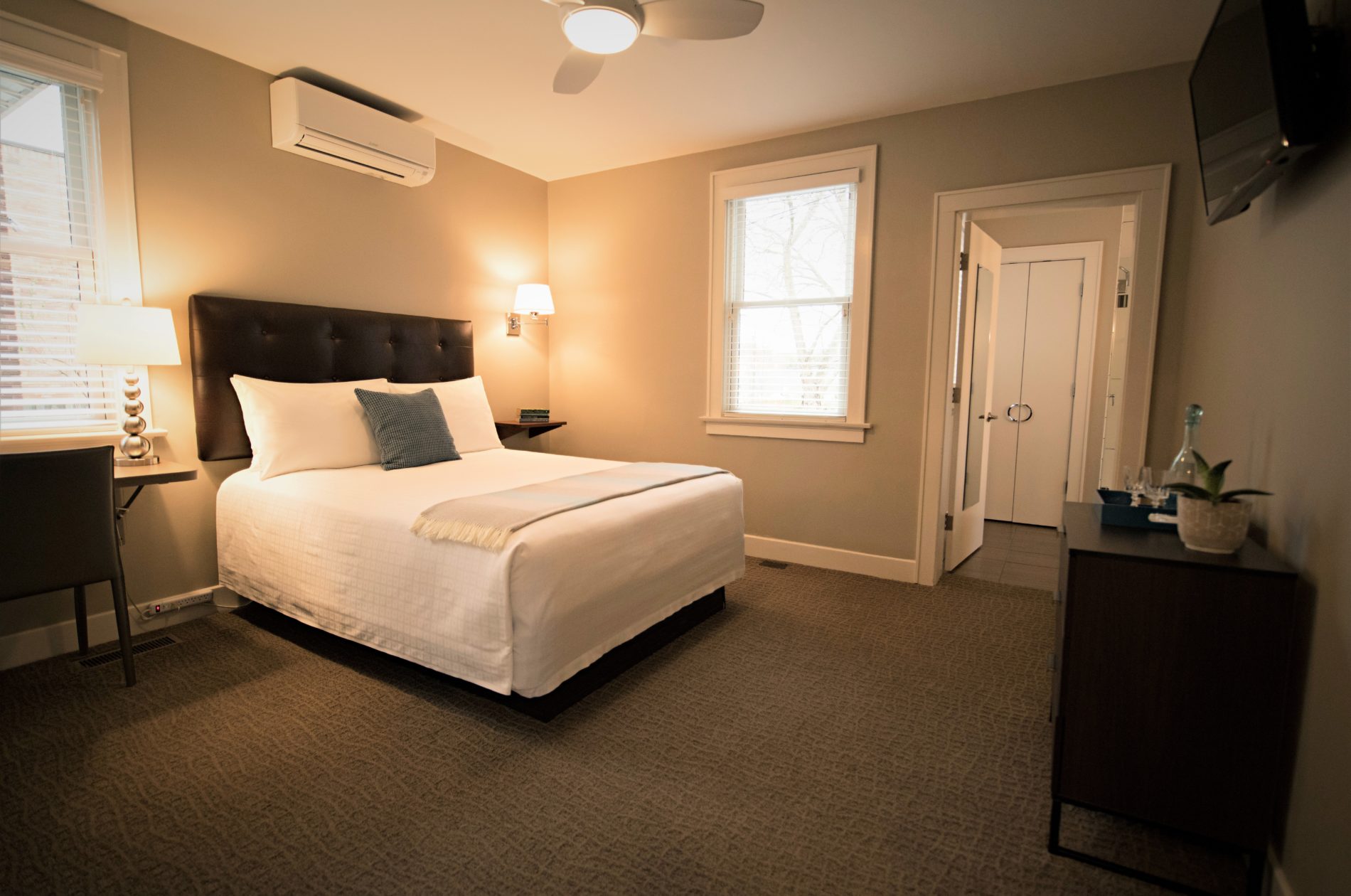 Looking into Room Two with view of desk, bathroom, and bed made with white linens and blue accent pillows