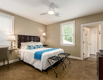 Looking into Room Two with view of desk, bathroom, and bed made with white linens and blue accent pillows