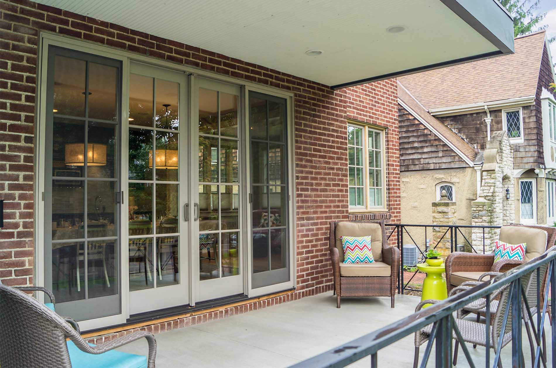 Exterior sitting area with wicker furniture and decorative pillows with view inside through glass double doors.