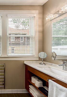 Bathroom showing open shelf teak vanity and white linens underneath marble counter-top.