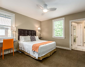 Looking into Room Five with view of desk, and bed made with white linens and orange accents