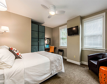 Looking into Room One with view of desk, orange parsons chair, television and brown club chair