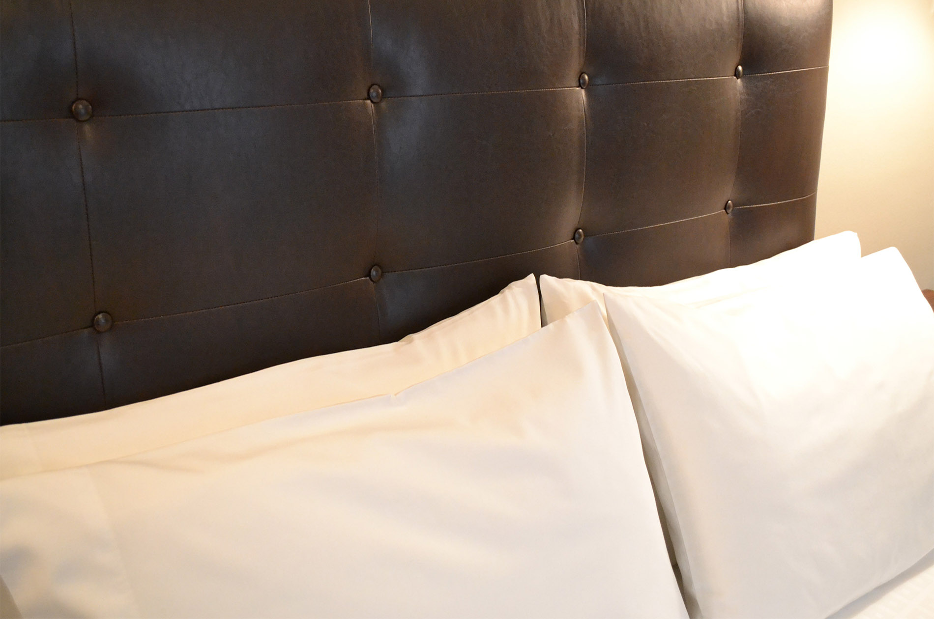 Dark brown headboard of bed contrasted with fluffy white pillows.