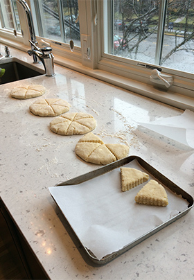 Rounds of scone dough cut into triangles with some on white parchment ready to bake